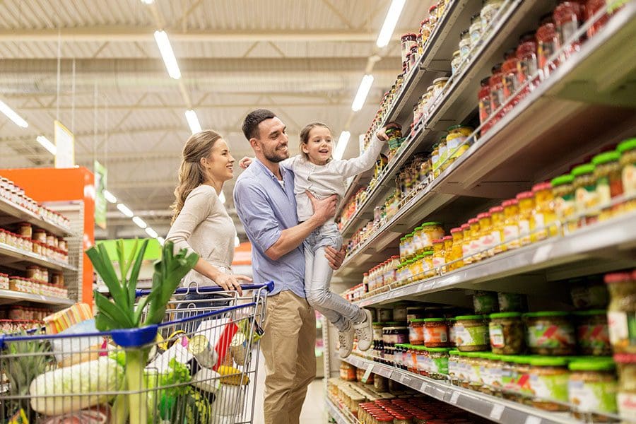 Consumer-Packaged Goods (CPG) Industry Programs - Father Lifting up Daughter To Top Shelf to Grab a Salsa in a Grocery Store Isle While Mom Watches with Cart