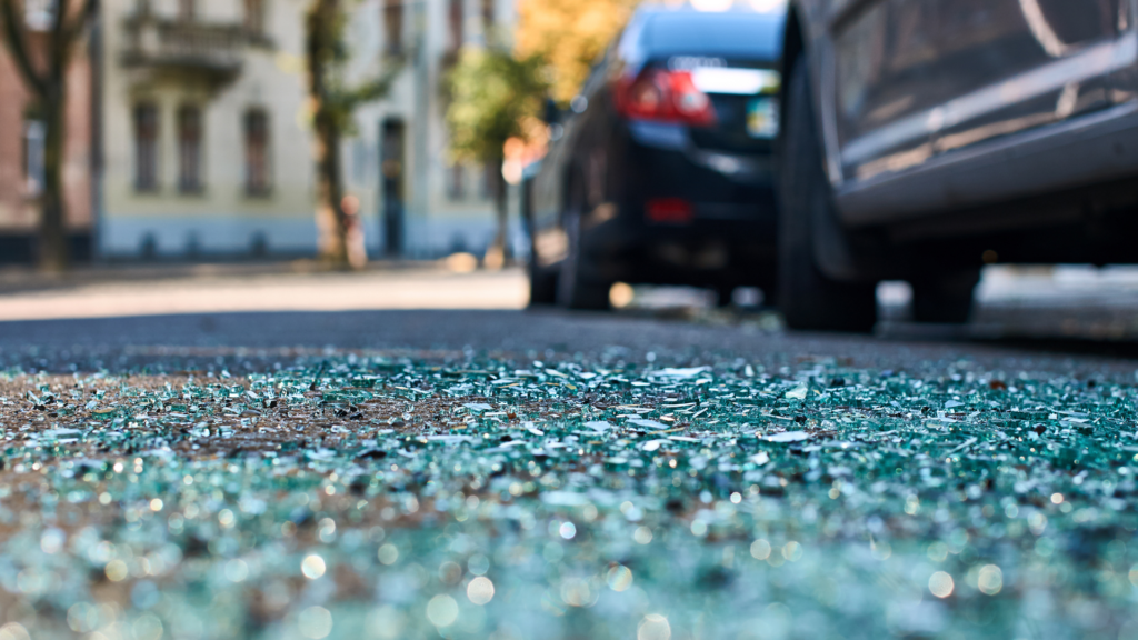 Uninsured Motorist Insurance Shattered car glass on the road after a collision, with shards scattered everywhere.
