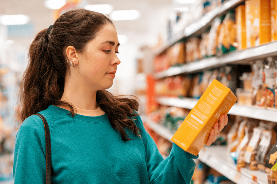 A woman in a grocery store aisle, carefully reading the information on a product package.